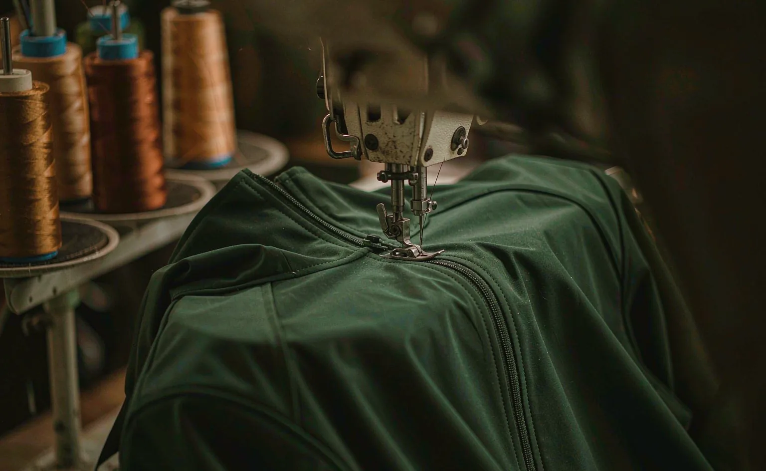 Industrial sewing machine stitching a forest green jacket seam